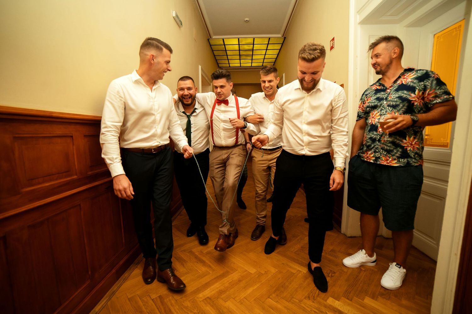 Group of formally dressed guests gathering in a wood-paneled hallway.