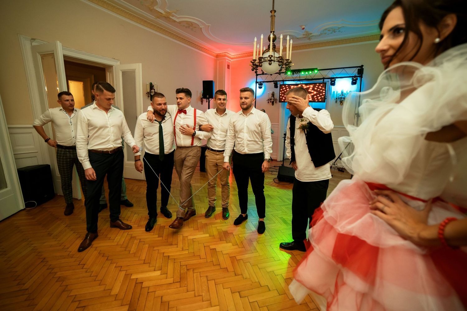 Party guests dancing under colorful lighting on a parquet floor.