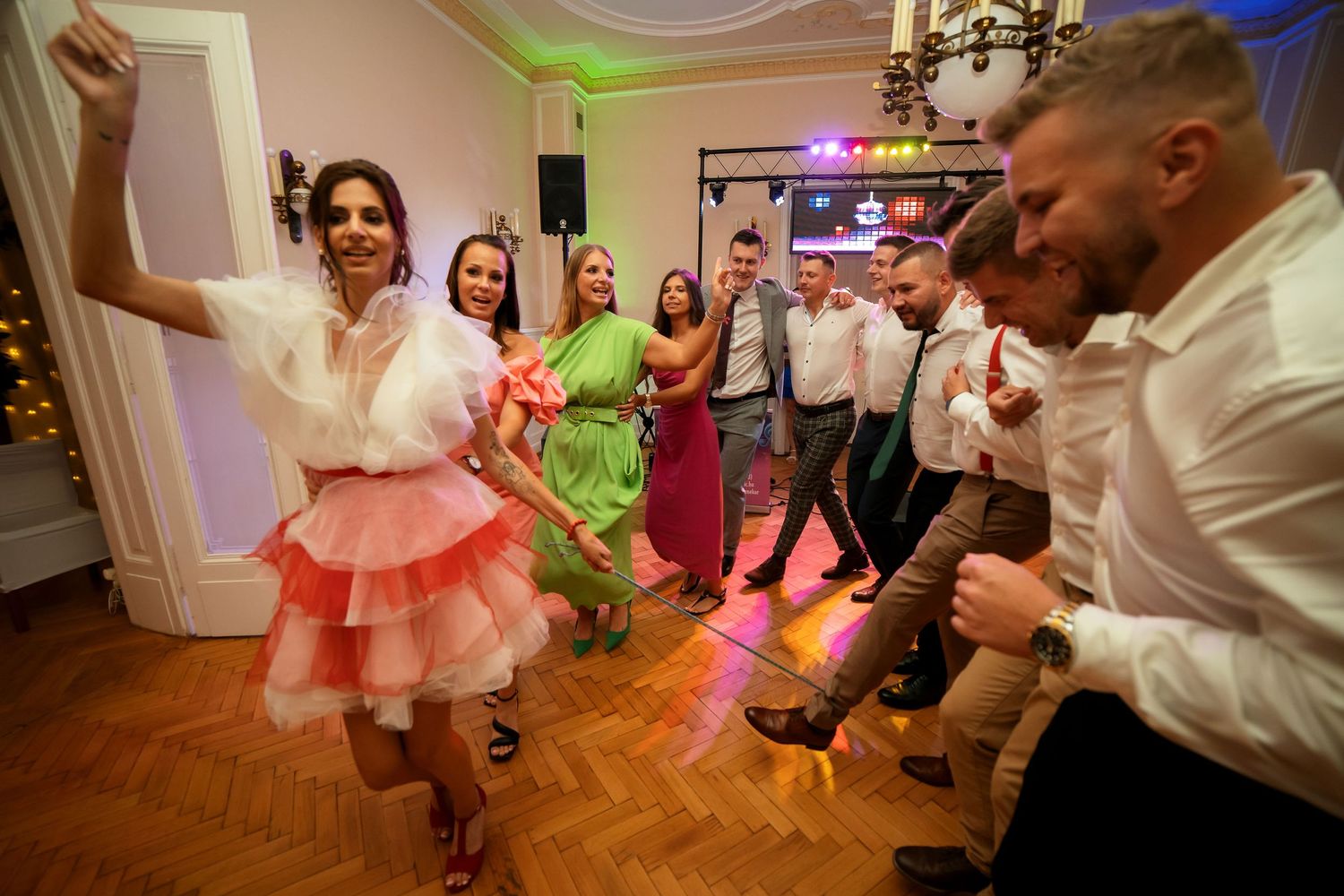 Dancers celebrate on parquet flooring under pink and blue lighting.