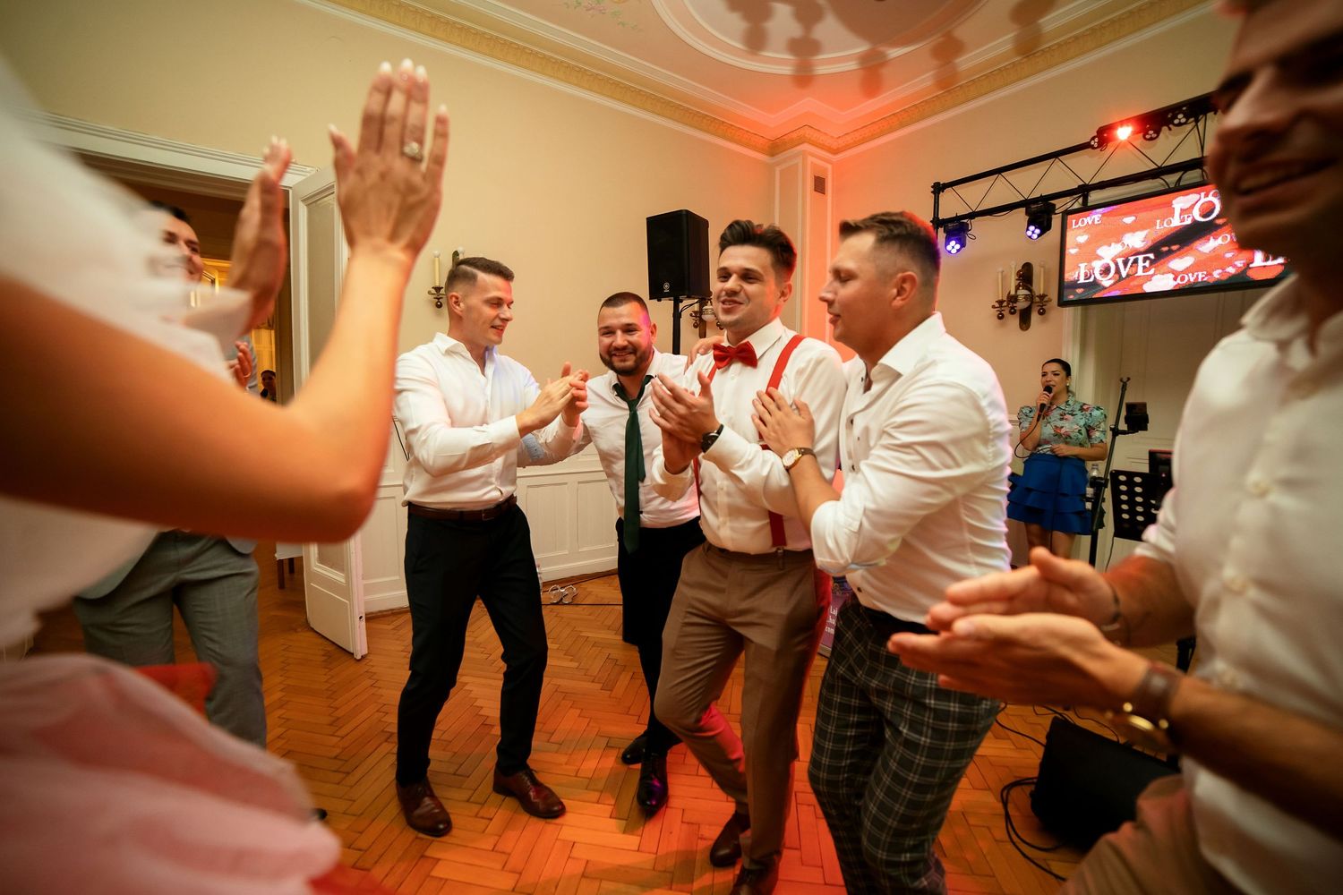Party guests in white shirts dance enthusiastically on wooden flooring under neon lights.