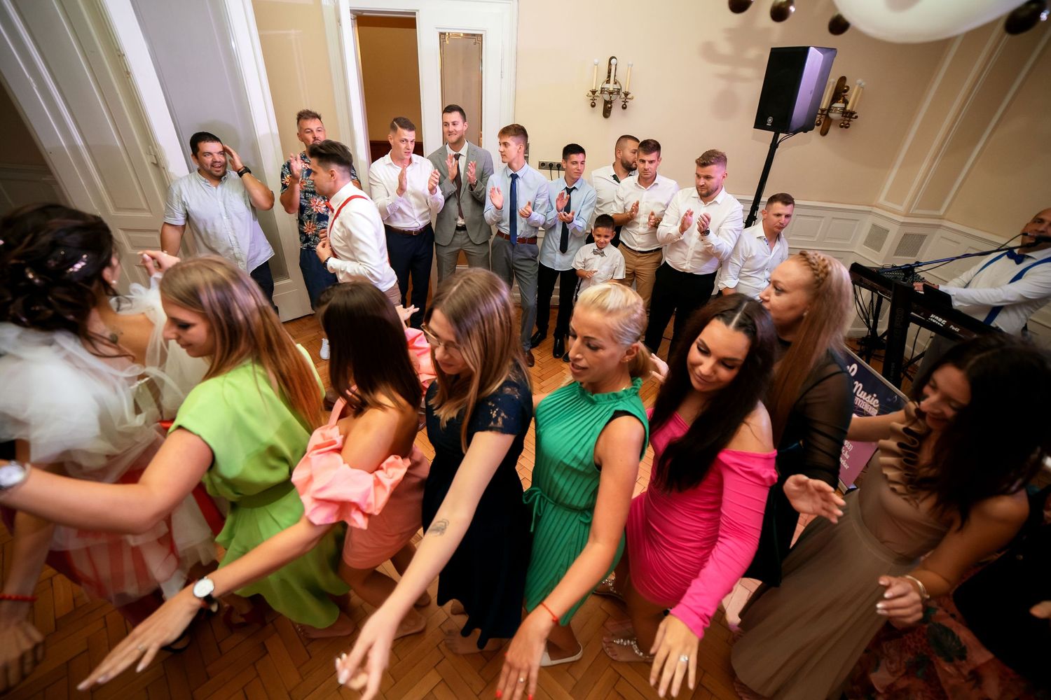 Wedding guests in bright summer attire dancing and celebrating at an indoor reception.