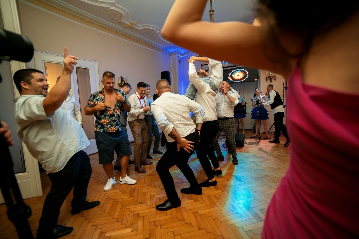 Enthusiastic dancers perform synchronized moves on a parquet dance floor with festive lighting.
