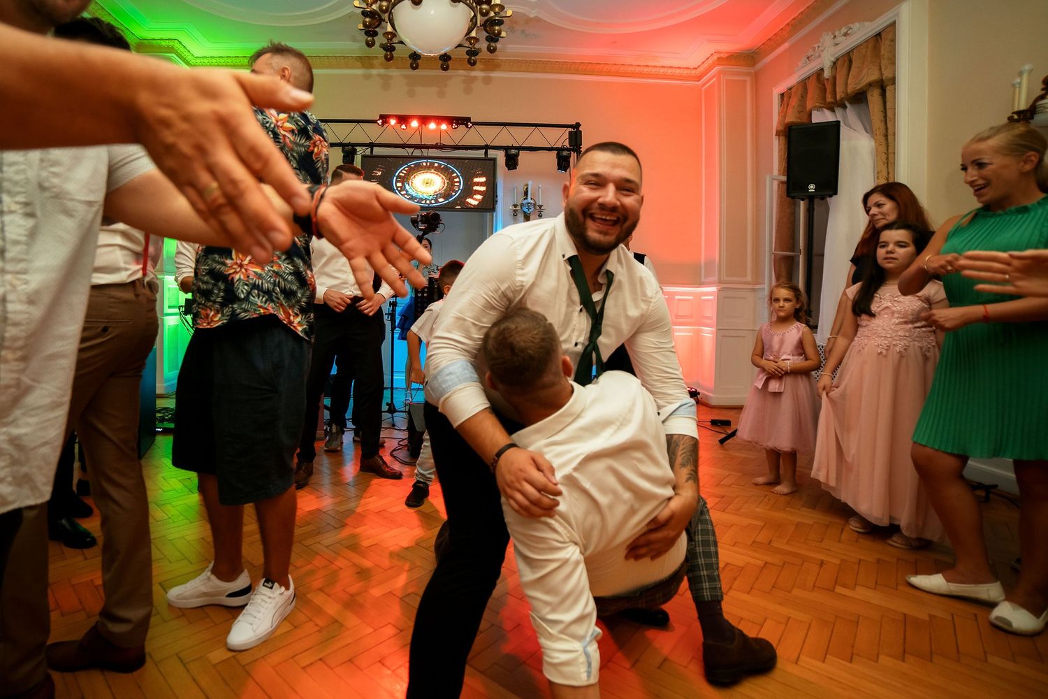 Lively dancers perform energetic moves during a wedding reception on hardwood floors.