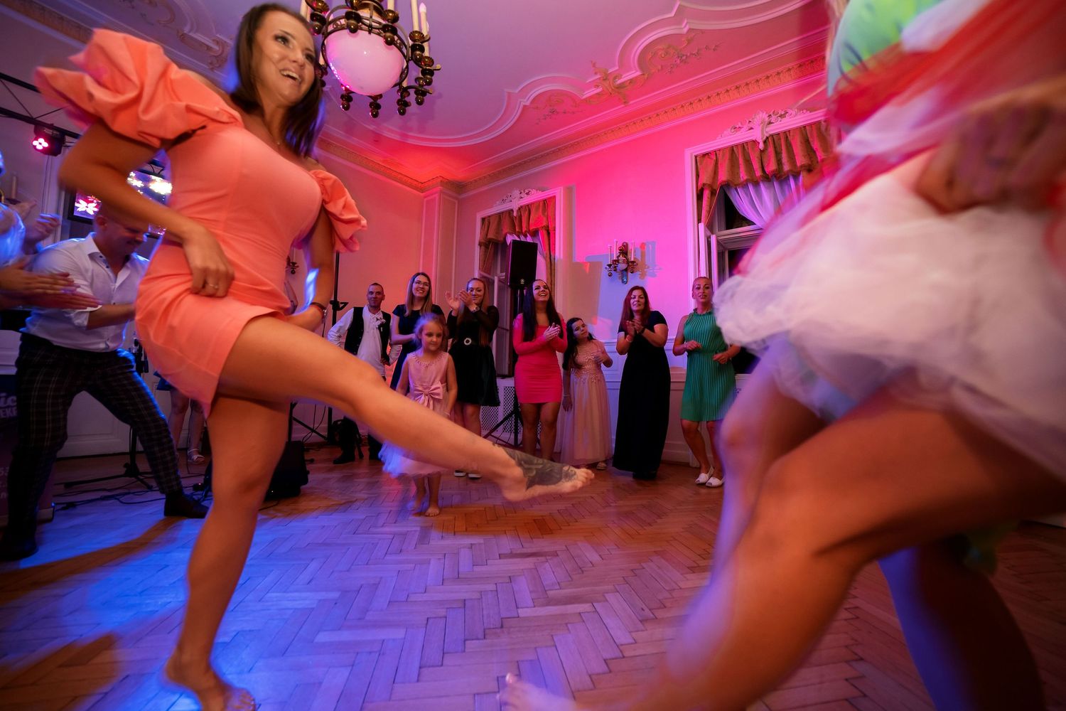 Dynamic dance moves captured during a wedding reception with dramatic pink and blue lighting.