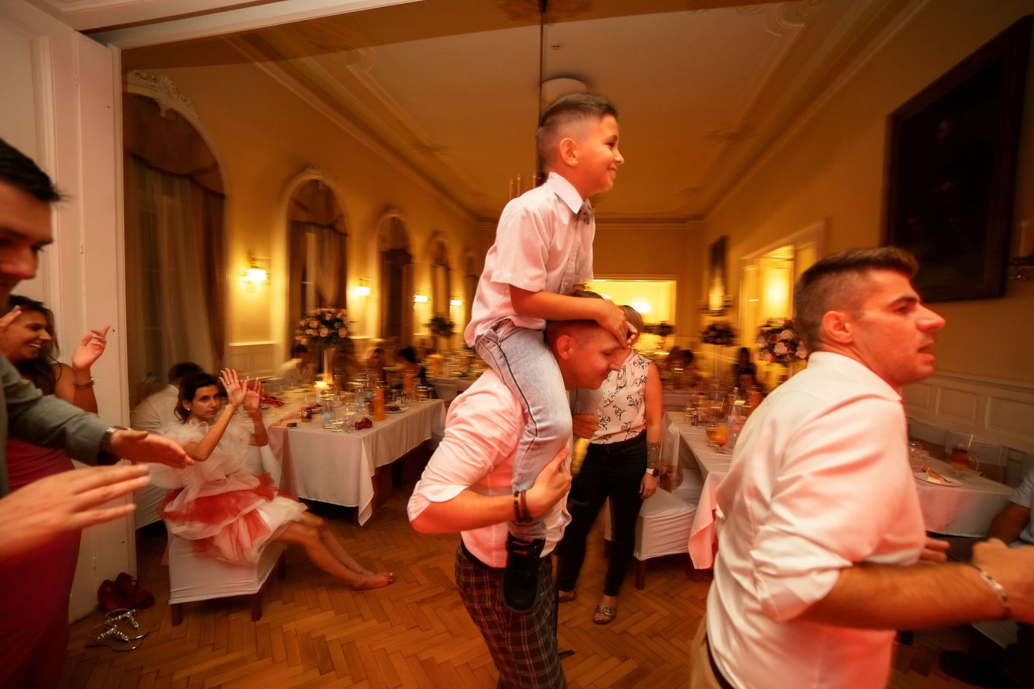 Wedding guests celebrate with enthusiastic dance moves at an elegantly lit indoor reception venue.