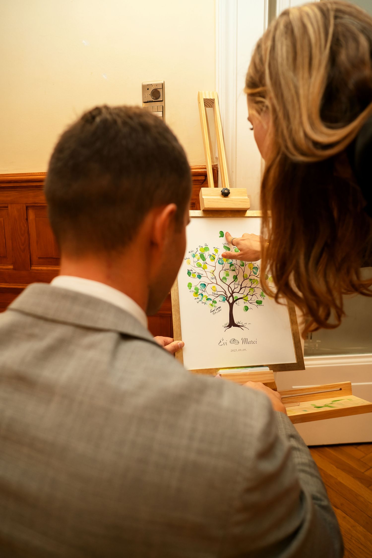 Couple viewing a decorative tree illustration at a wedding guestbook station.