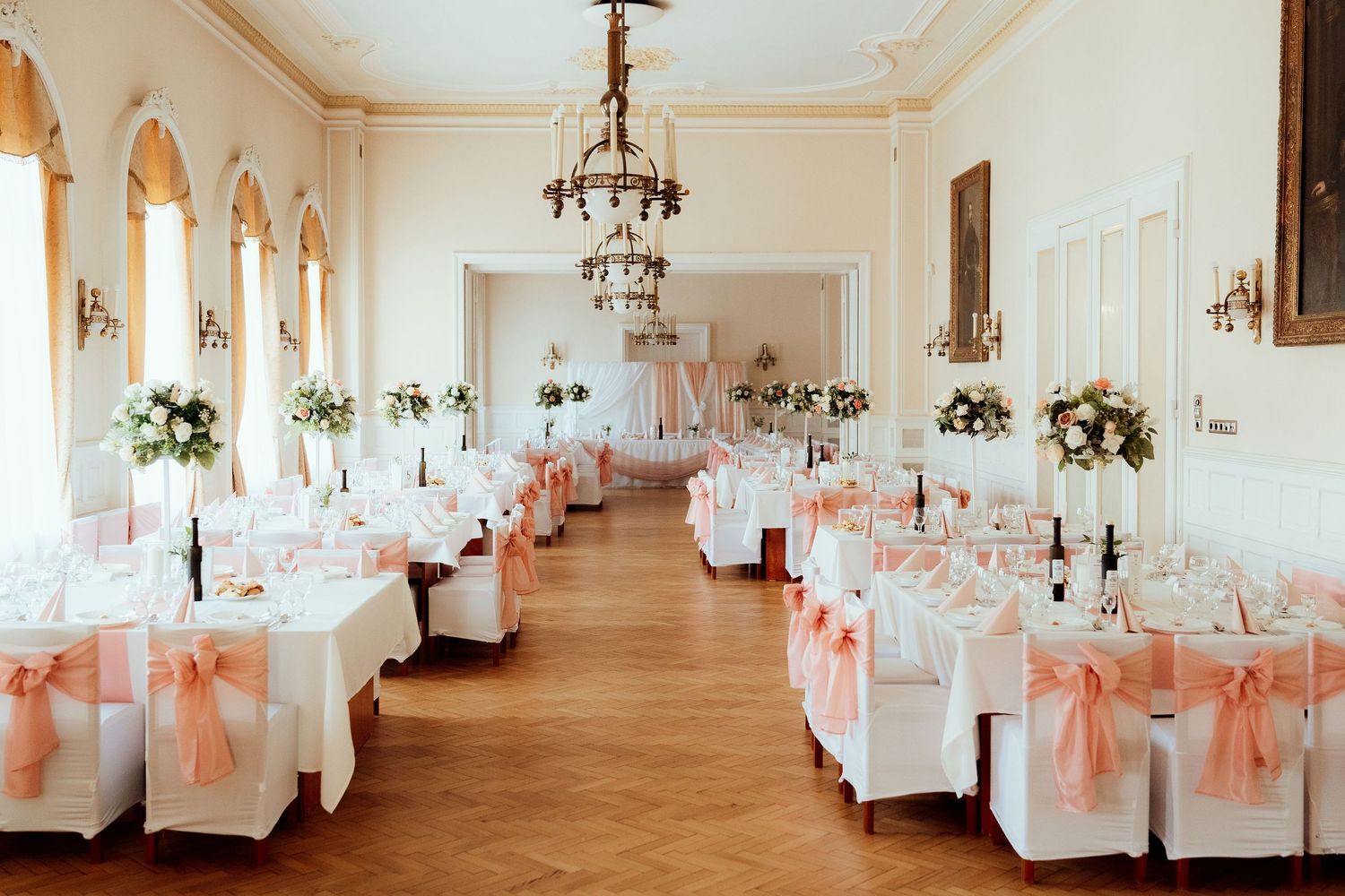 Long elegant banquet hall with white chairs adorned with peach sashes and floral decorations.