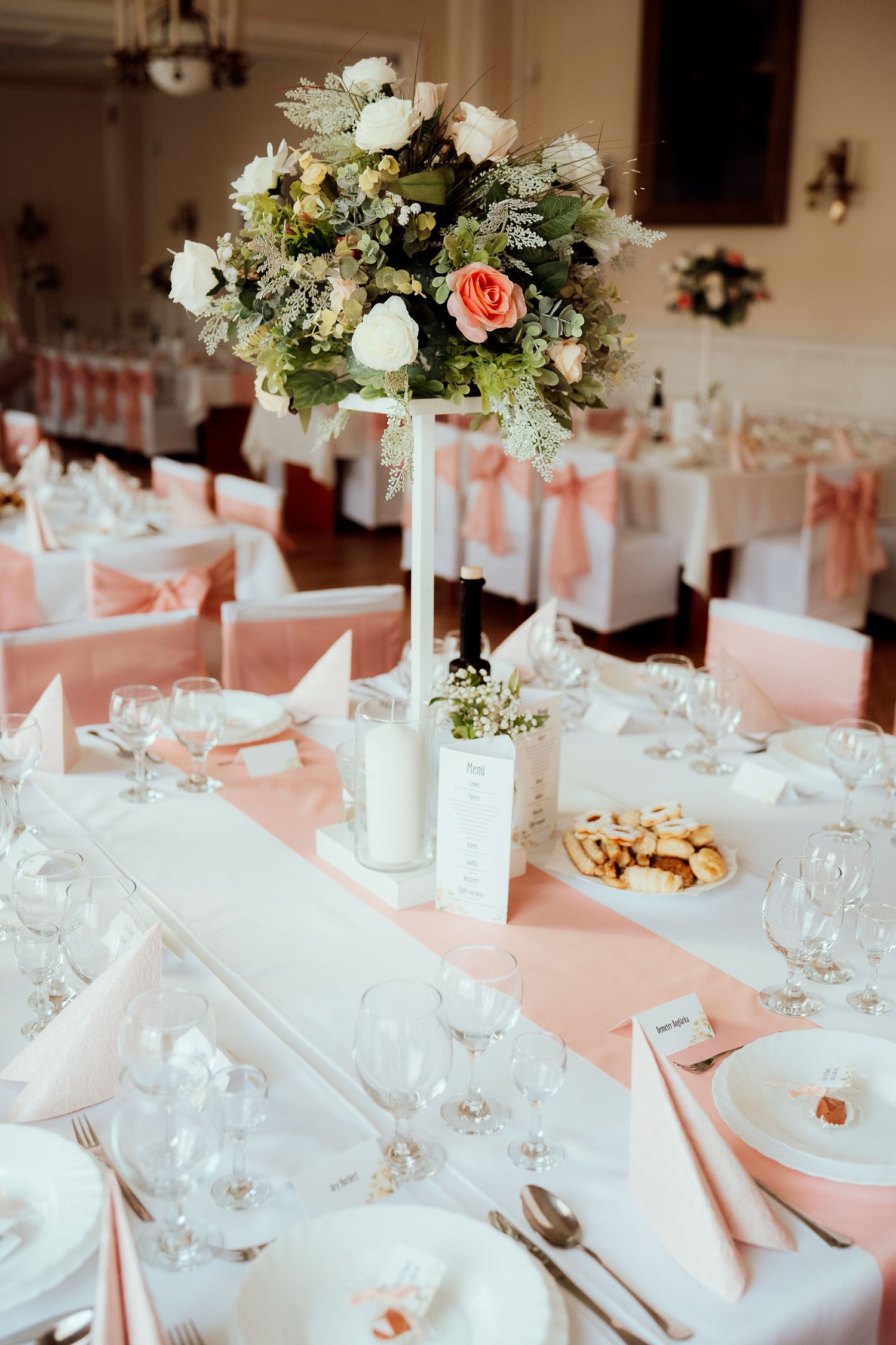 Elegant wedding table setting with tall white and coral floral centerpiece and peach table runners.