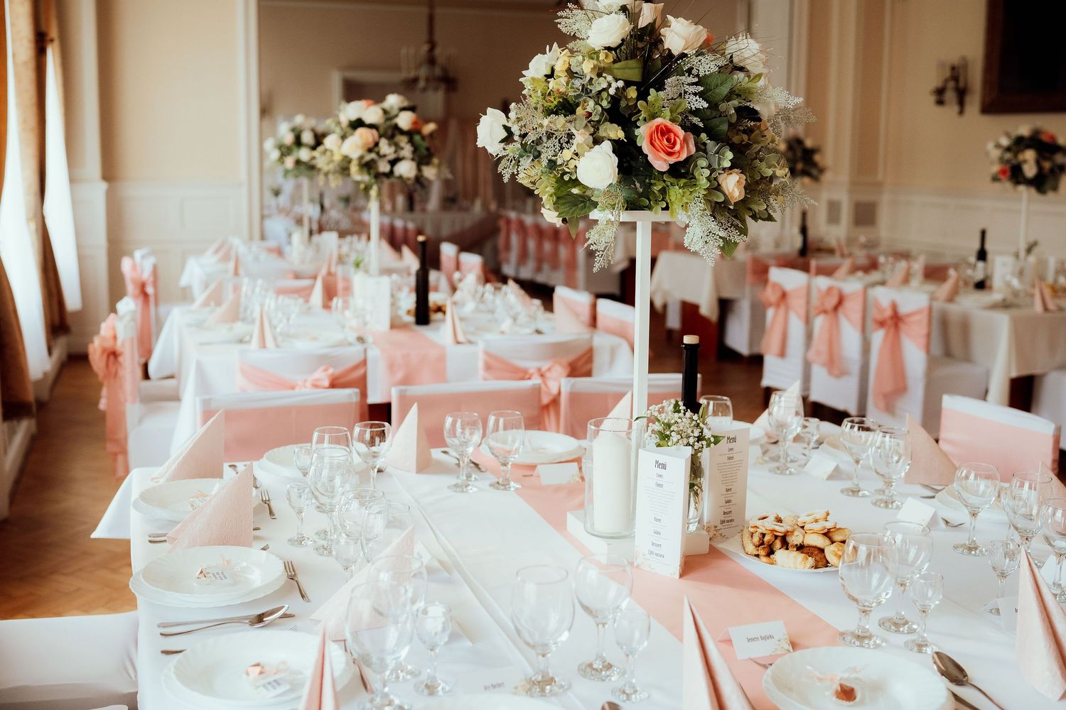 Wedding reception tables decorated in white and peach with tall floral centerpieces and crystal glassware.