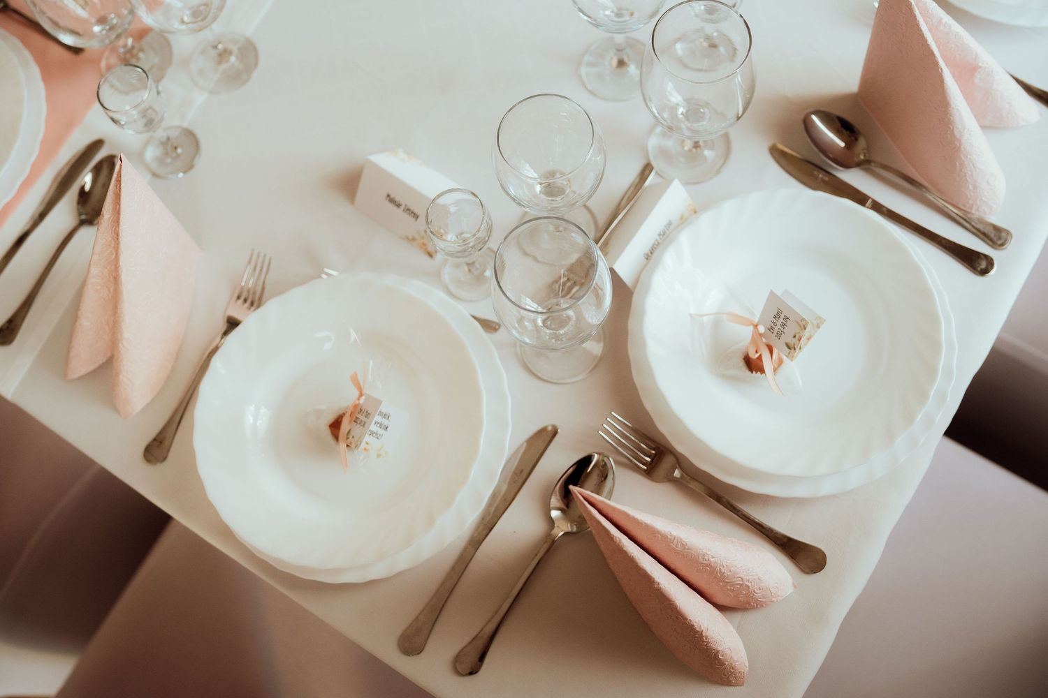 Close-up of formal place setting with white plates, crystal glasses and peach napkins.