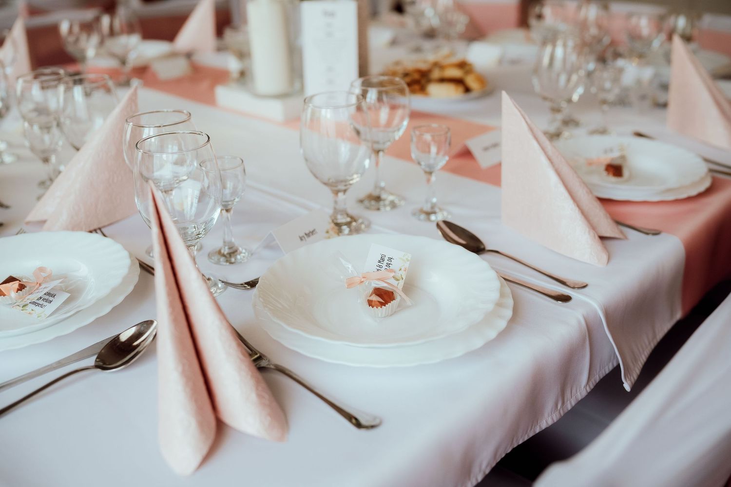 Formal dining table setting with white plates, peach napkins and crystal stemware.