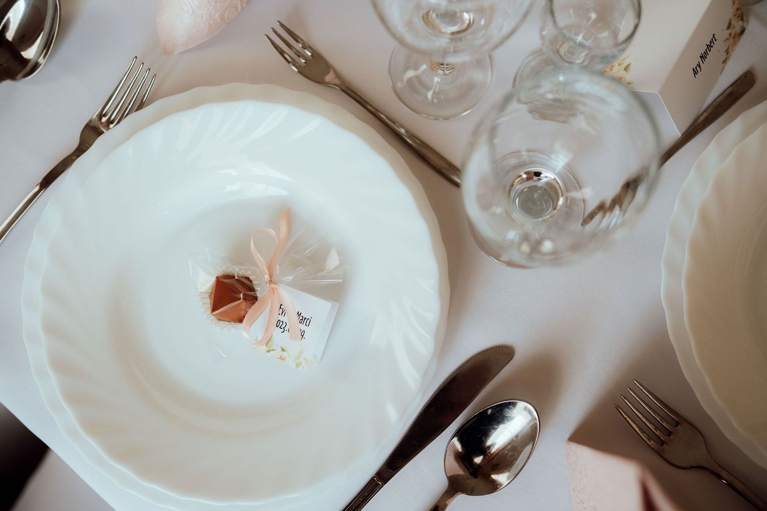 White dinner plate with delicate place setting and crystal glasses on formal table.