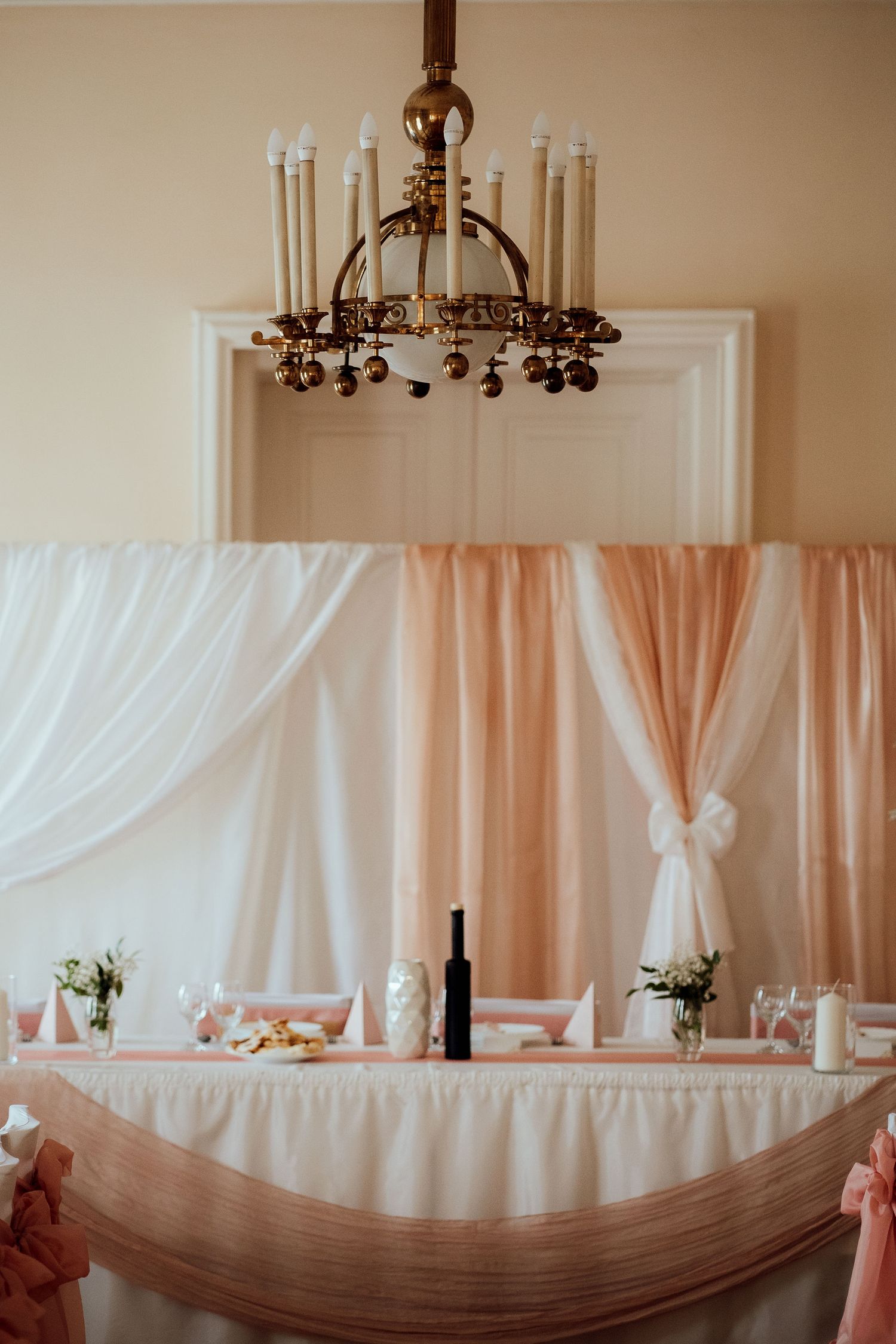 Vintage chandelier above elegant head table with peach and white draped fabric backdrop.