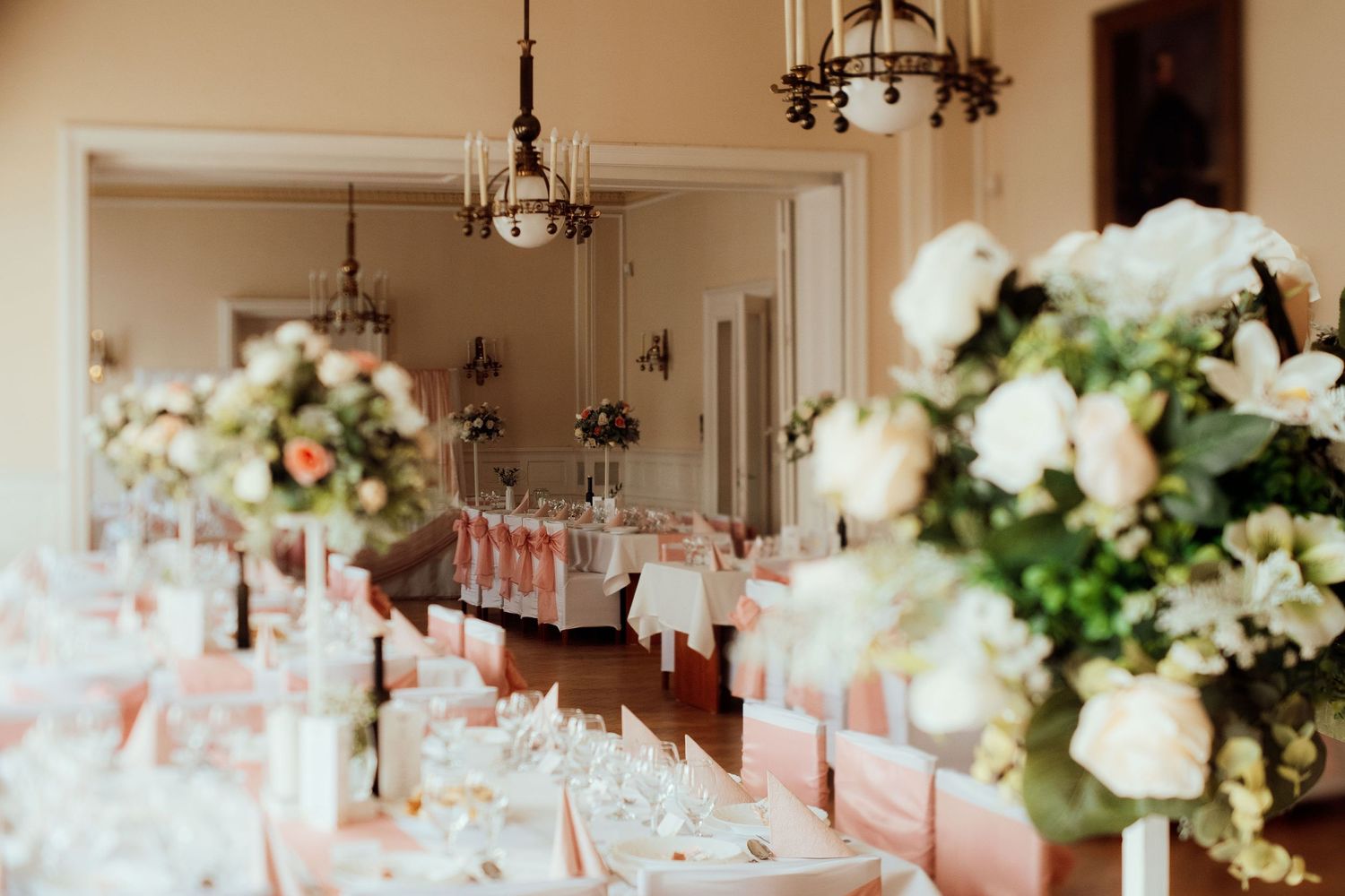 Banquet hall with crystal chandeliers and tables decorated with tall floral centerpieces.
