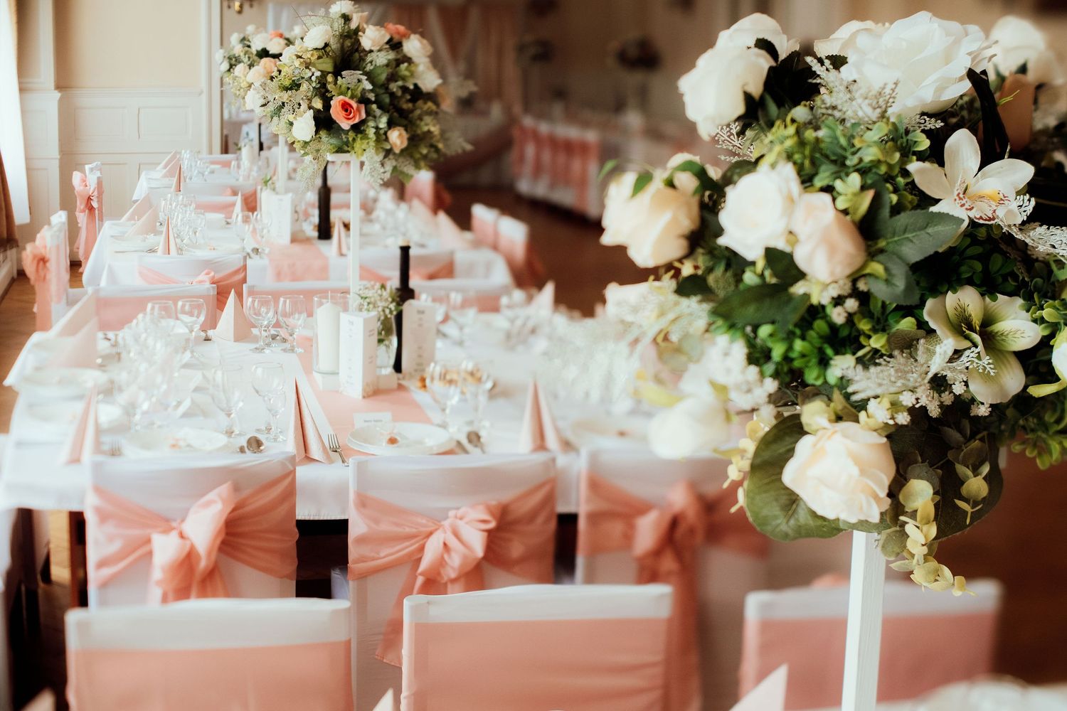 Elegant wedding reception tables decorated with white chairs, pink sashes and floral centerpieces.
