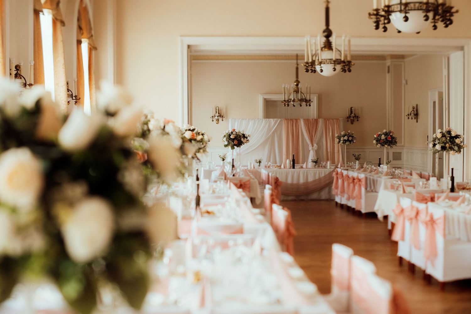 Luxurious wedding venue with chandeliers and tables decorated in pink and white.