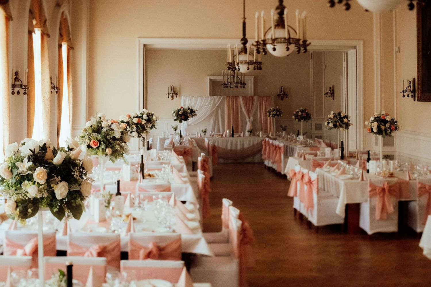 Spacious ballroom set for wedding reception with pink accents and white floral arrangements.
