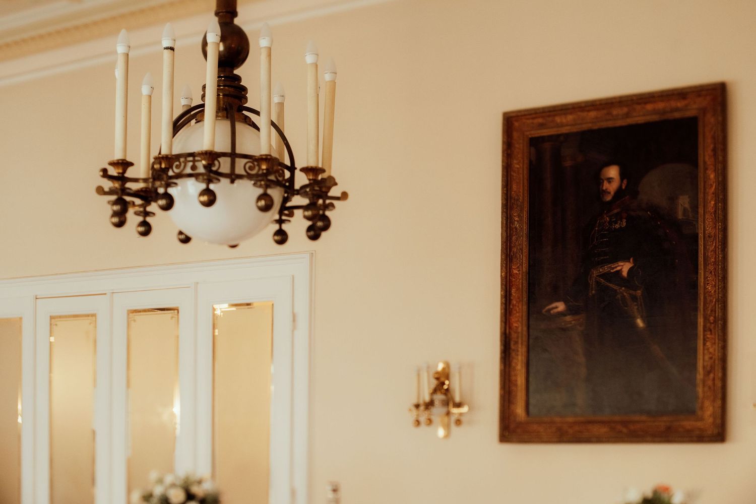 Vintage chandelier and classical portrait painting adorning an elegant cream-colored wall.