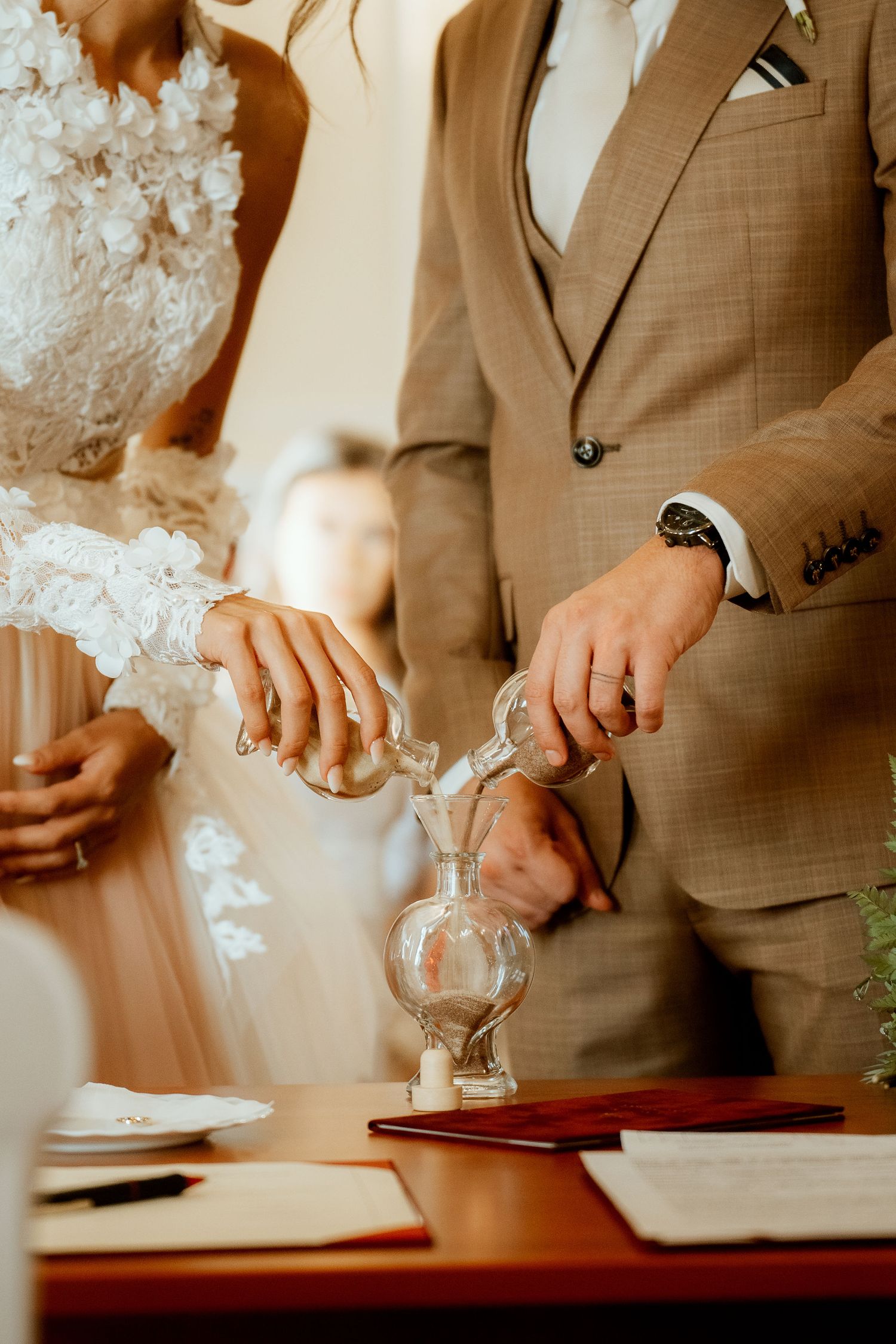 Close-up of ceremonial sand pouring ritual with tan suit and white dress details.