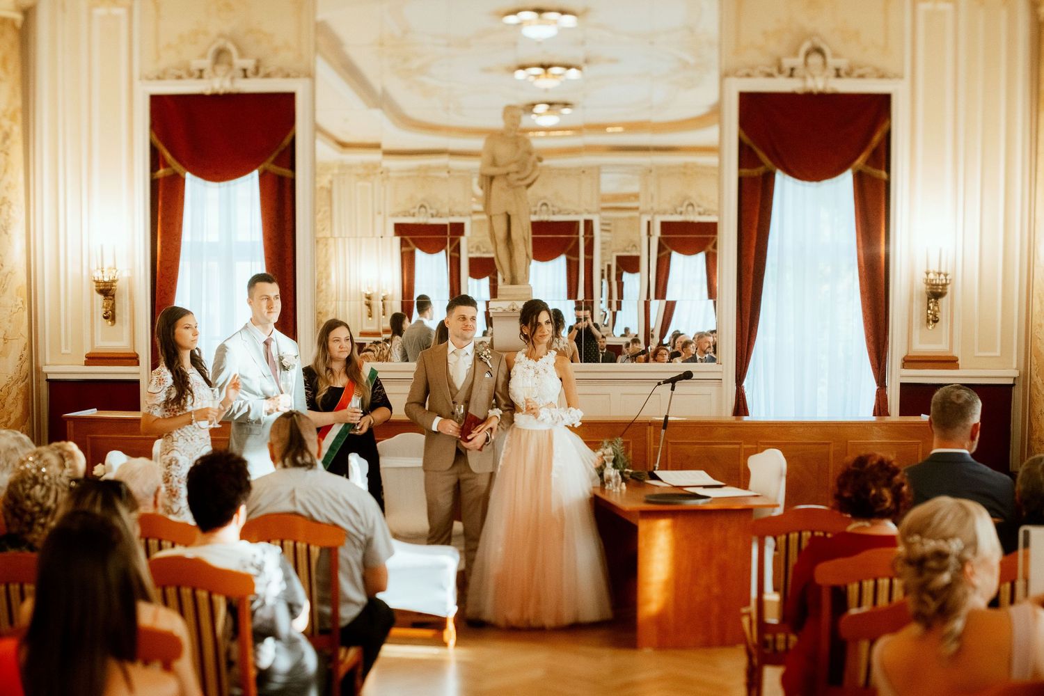 Wedding ceremony in an elegant historic ballroom with red curtains and ornate details.
