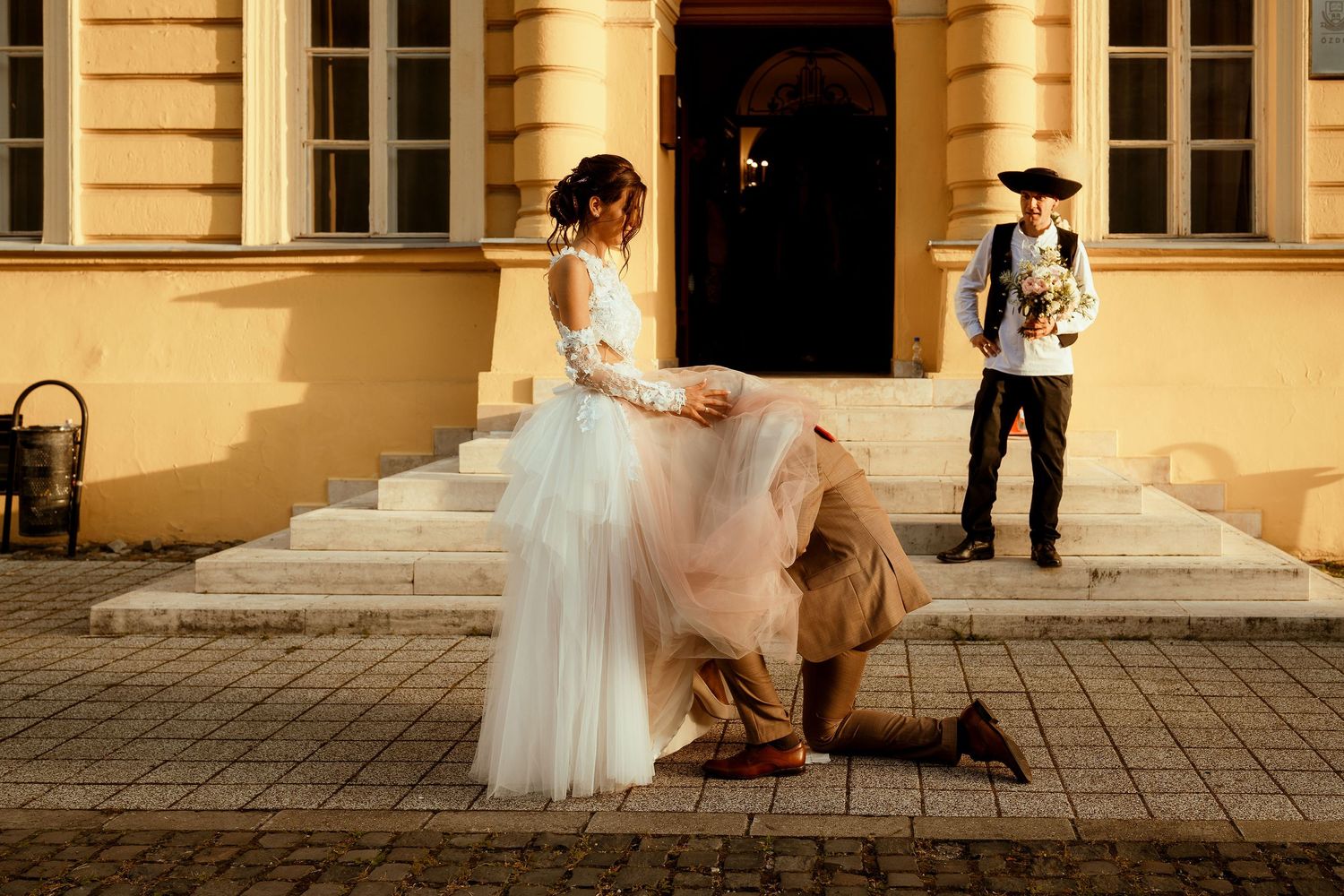 Wedding photoshoot on historic building steps with photographer in background.