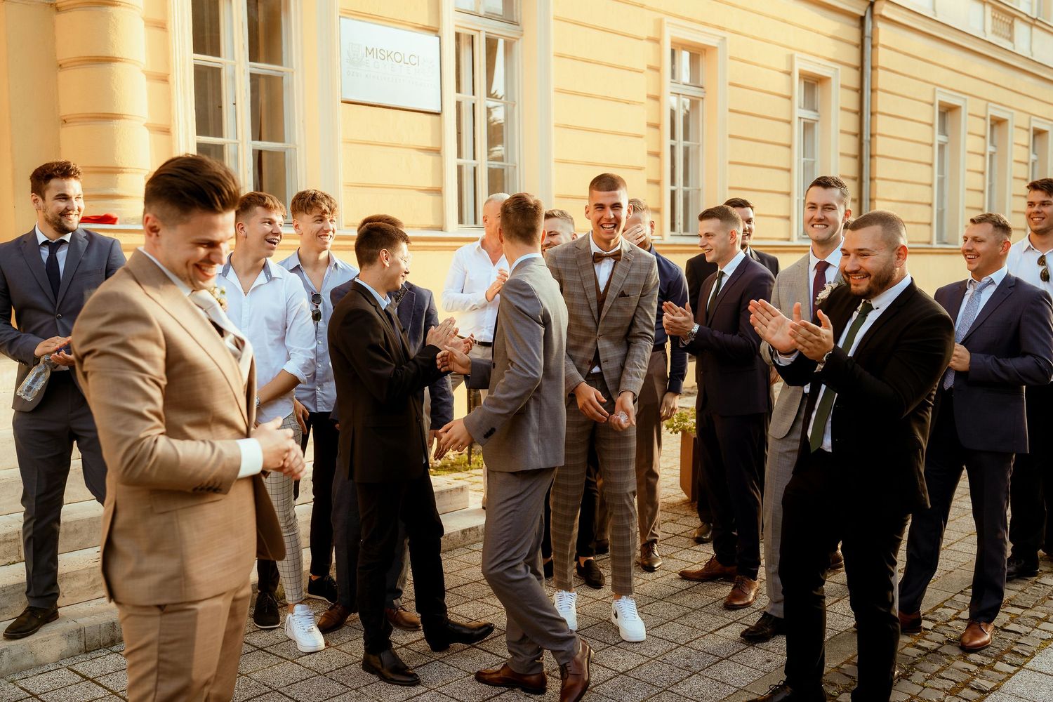 A group of well-dressed guests gather for a wedding celebration outside a historic building.