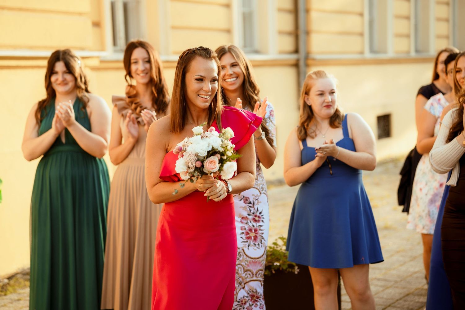 Wedding guests in elegant dresses applaud during an outdoor celebration.