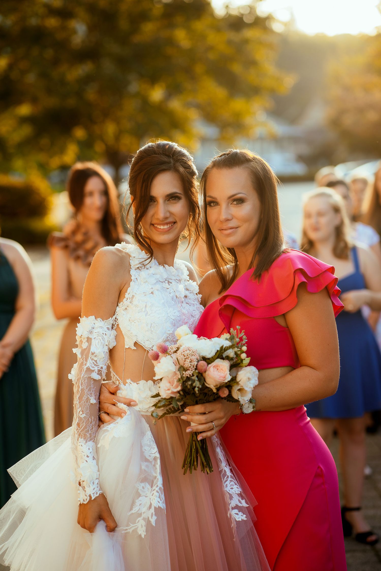 Two wedding attendees pose with a bouquet during golden hour celebrations.