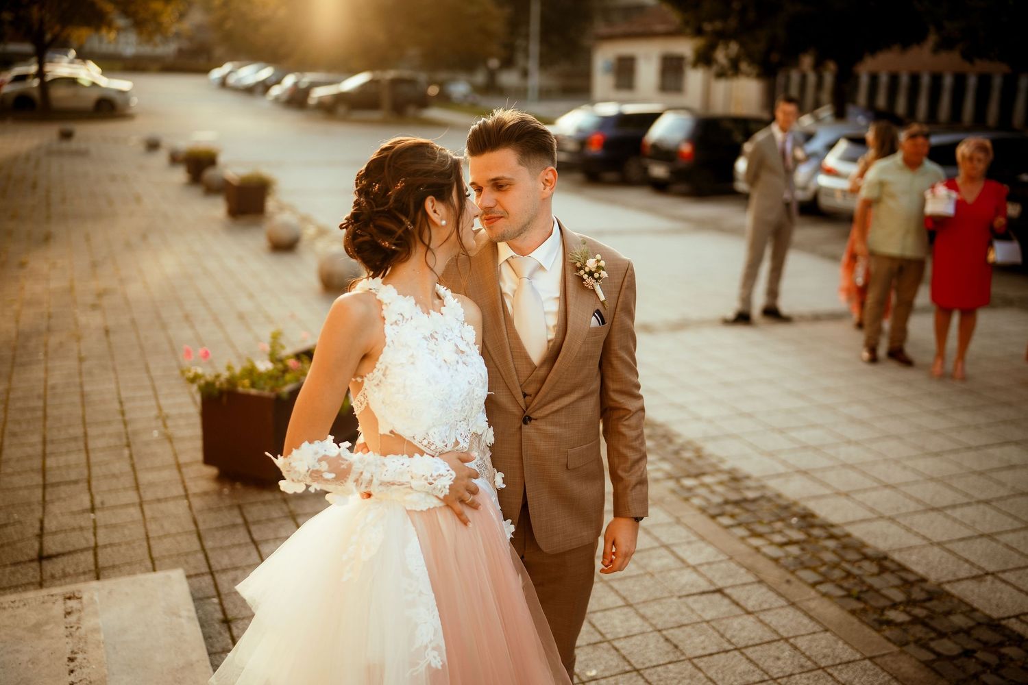 A romantic sunset portrait of newlyweds on a cobblestone street with guests in background.
