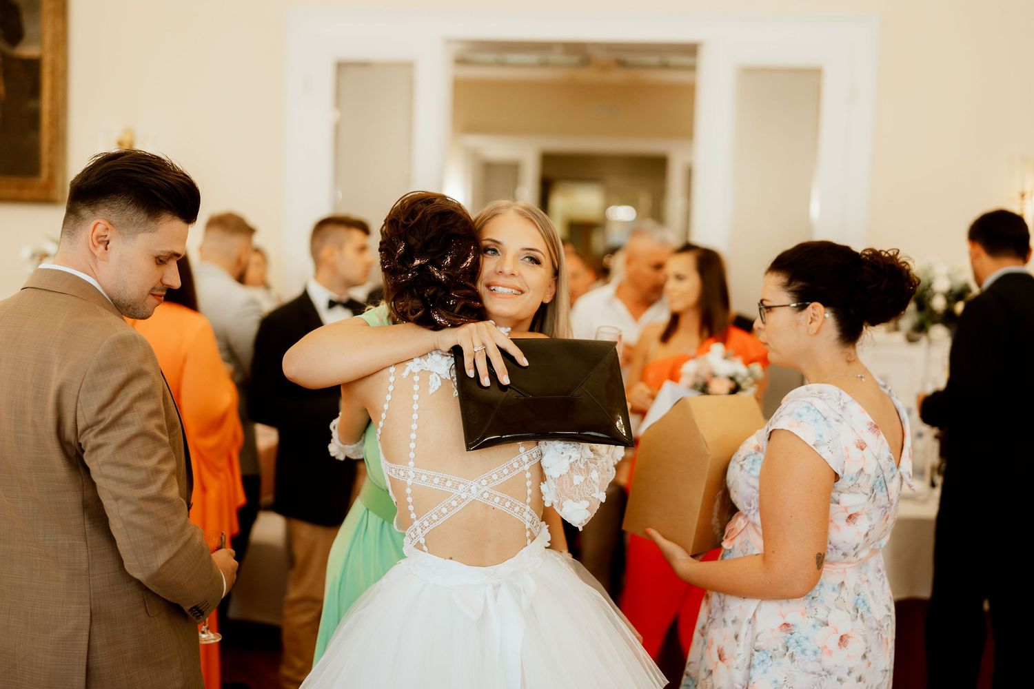 Wedding celebration guests sharing embraces and conversations at an indoor reception.