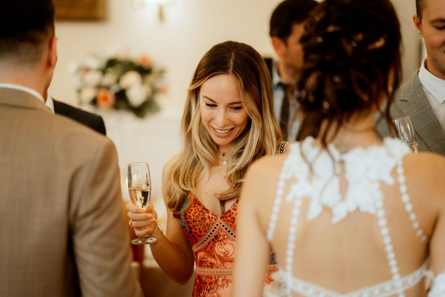 Wedding guests mingling and enjoying champagne during an indoor reception celebration.