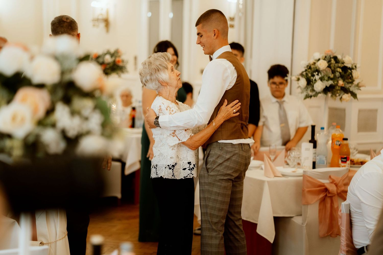 A heartfelt dance moment between guests at an elegant wedding reception with white floral decorations.