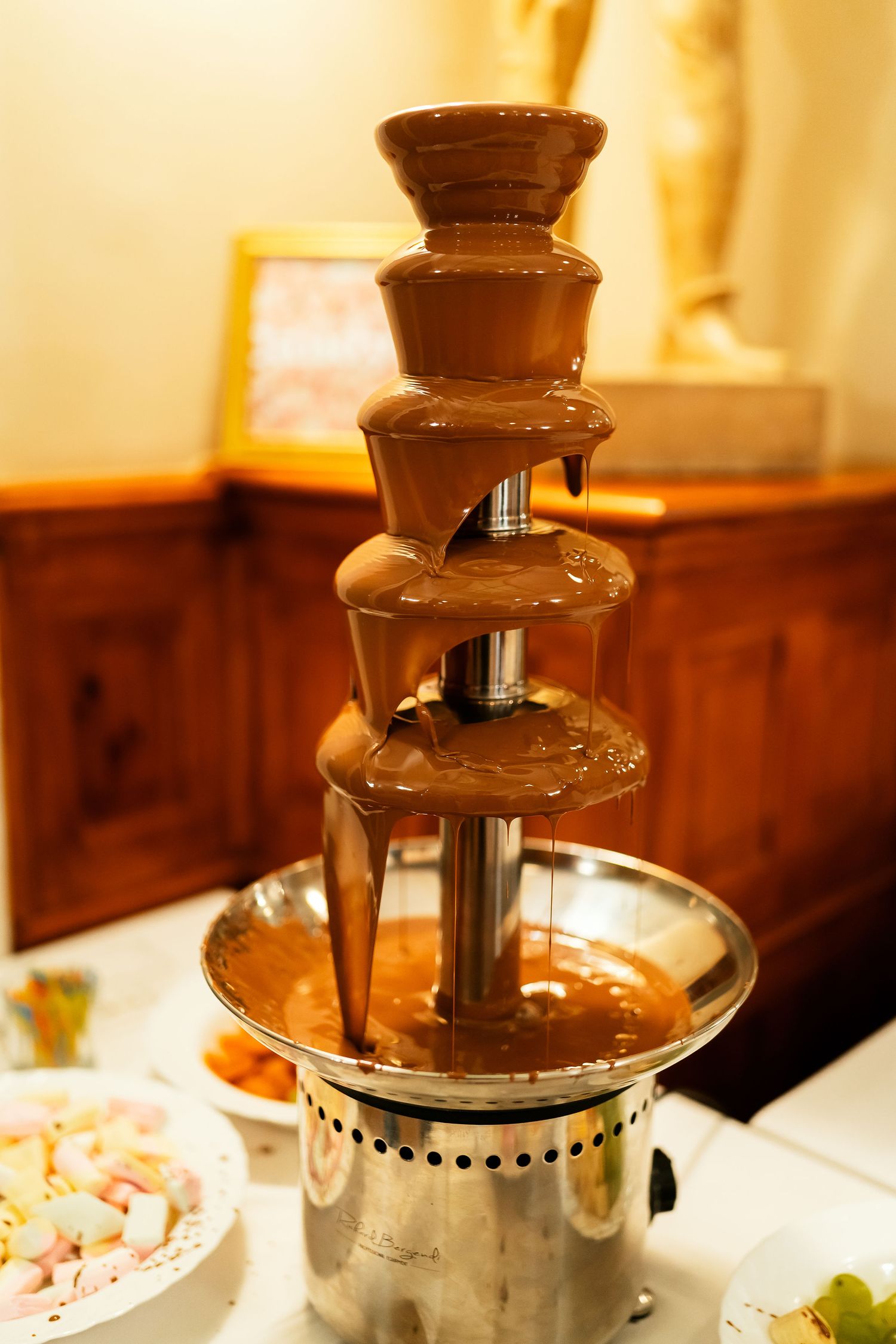 Elegant chocolate fountain display with multiple tiers flowing with melted chocolate at an event.