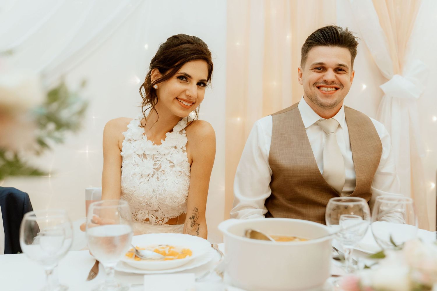 Couple seated at decorated wedding reception table sharing a joyful moment.