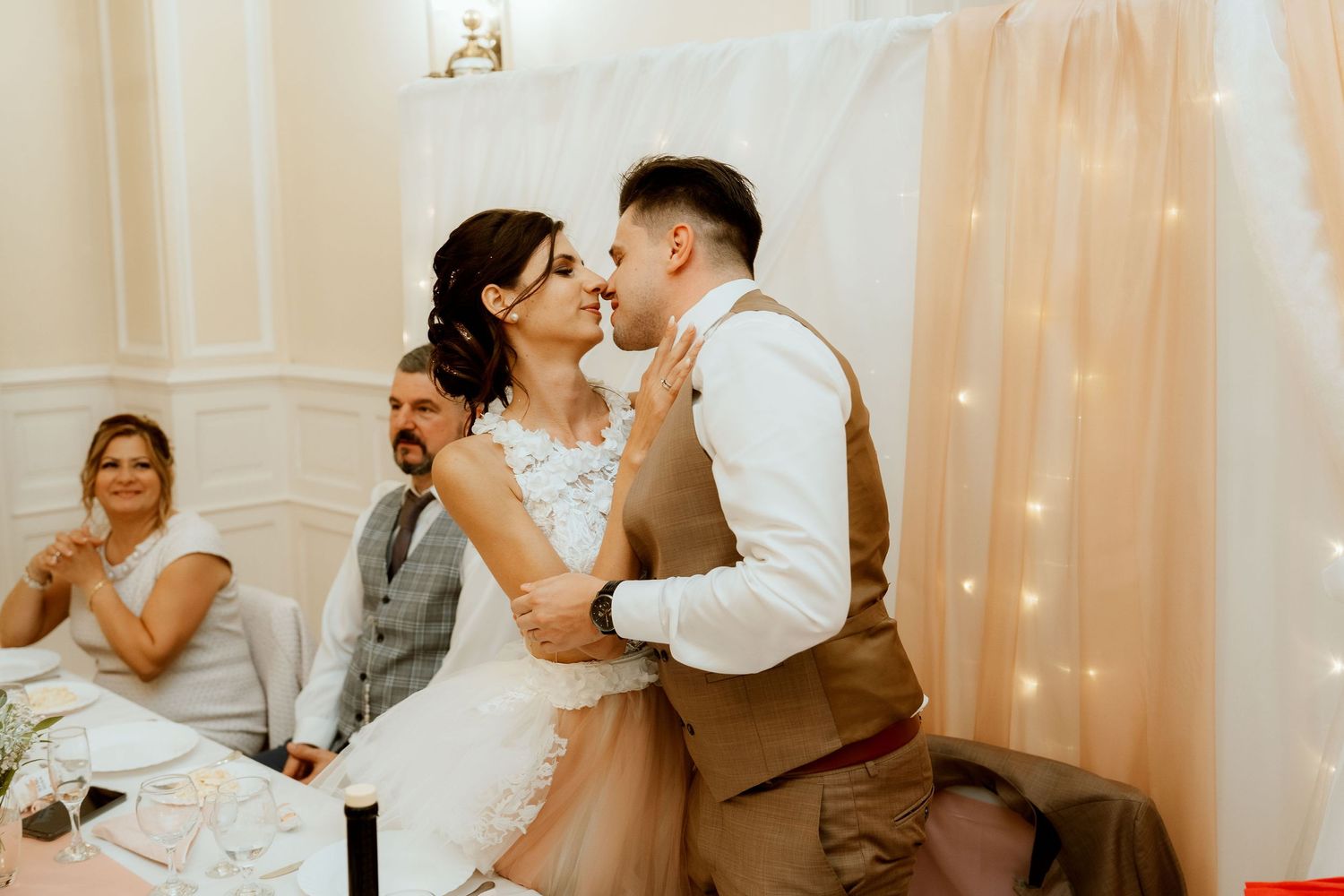 A romantic wedding dance moment with guests watching in the background under soft string lights and white decor.