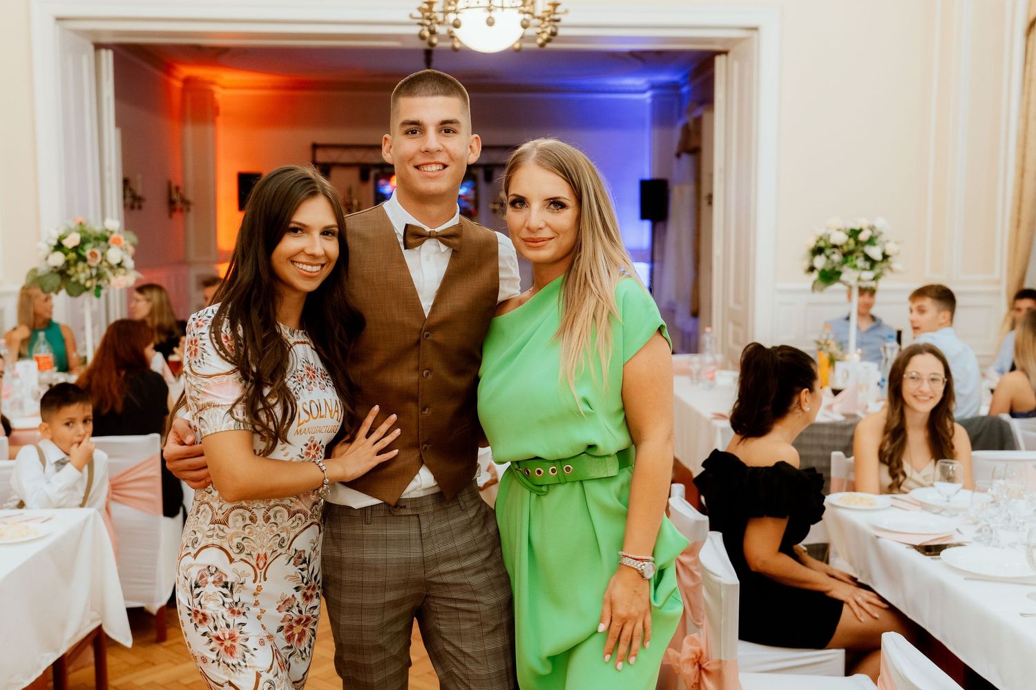 Wedding reception guests pose together in a banquet hall with blue and red lighting effects.
