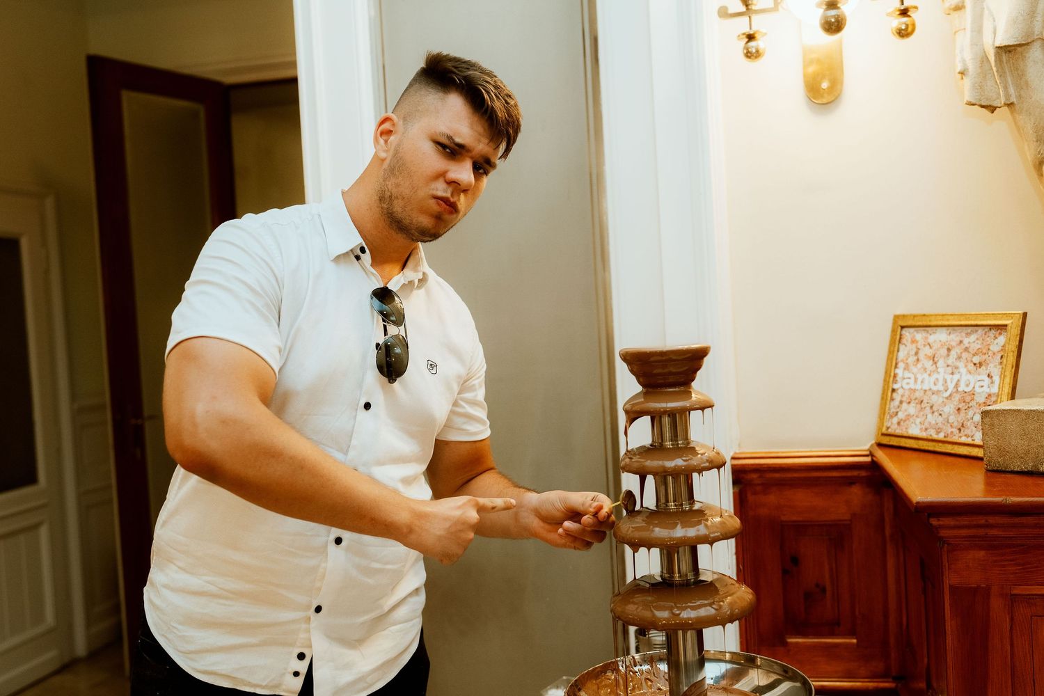 A person in white serves dessert from an elegant chocolate fountain display.