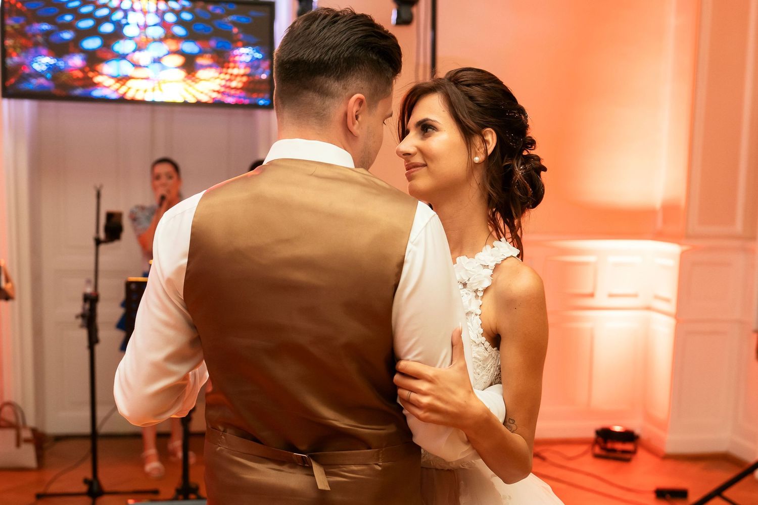 A couple shares an intimate slow dance moment at their wedding reception with pink lighting.