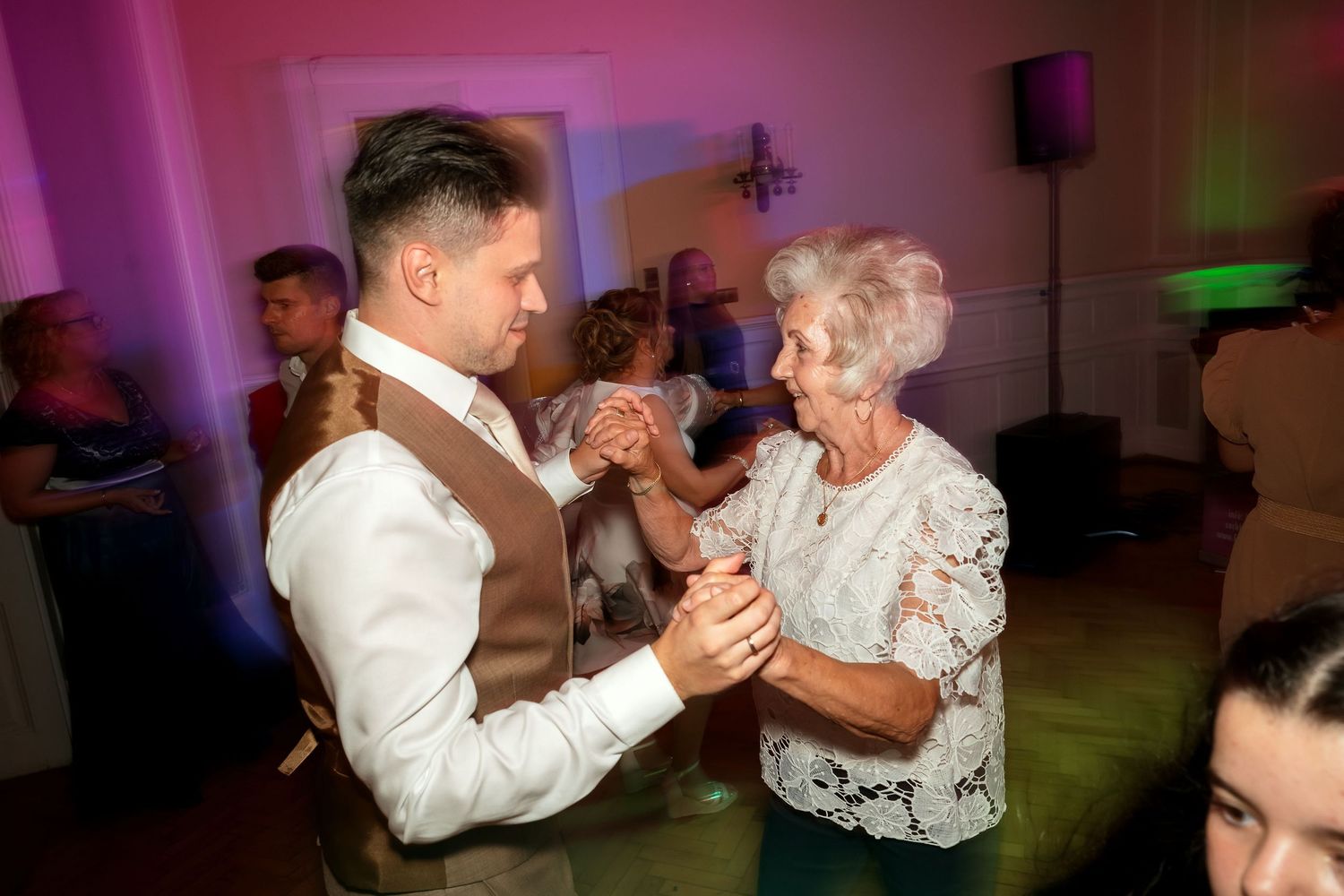 Guests share a dance under pink mood lighting at an indoor celebration.