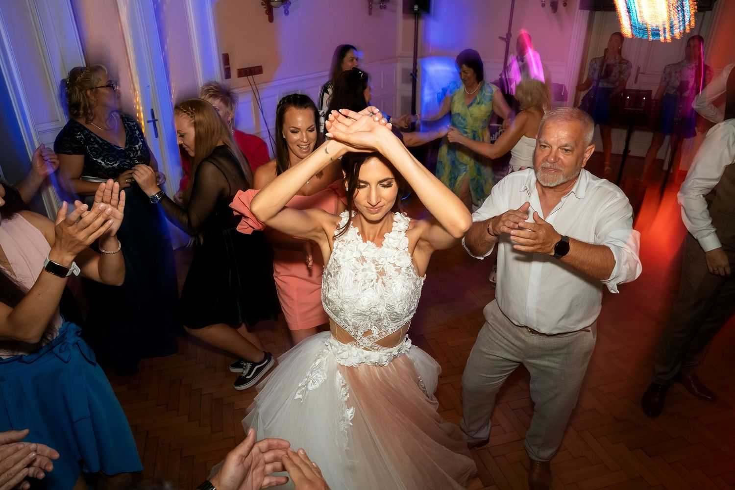 Wedding guests surround and celebrate with someone in a white gown on the dance floor.