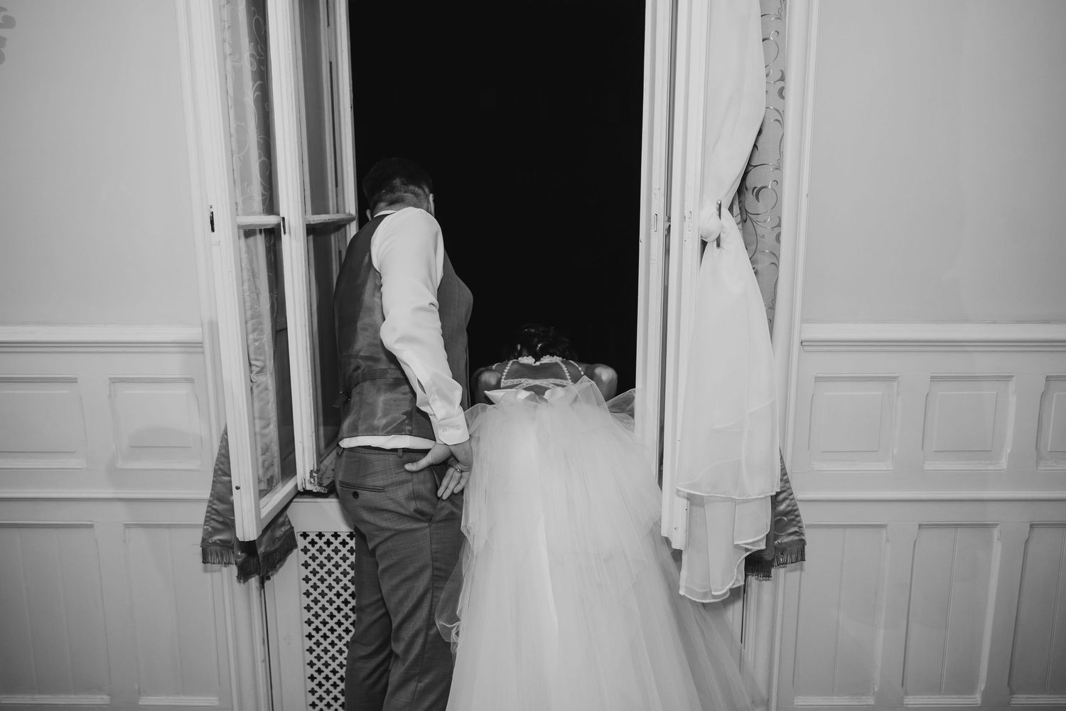 Artistic black and white image capturing intimate reception moments through doorways.