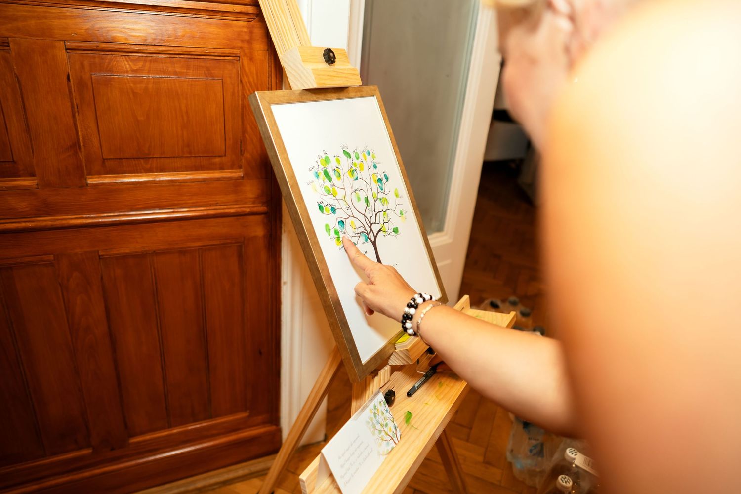 Artist working on a colorful tree painting on an easel next to a wooden cabinet.