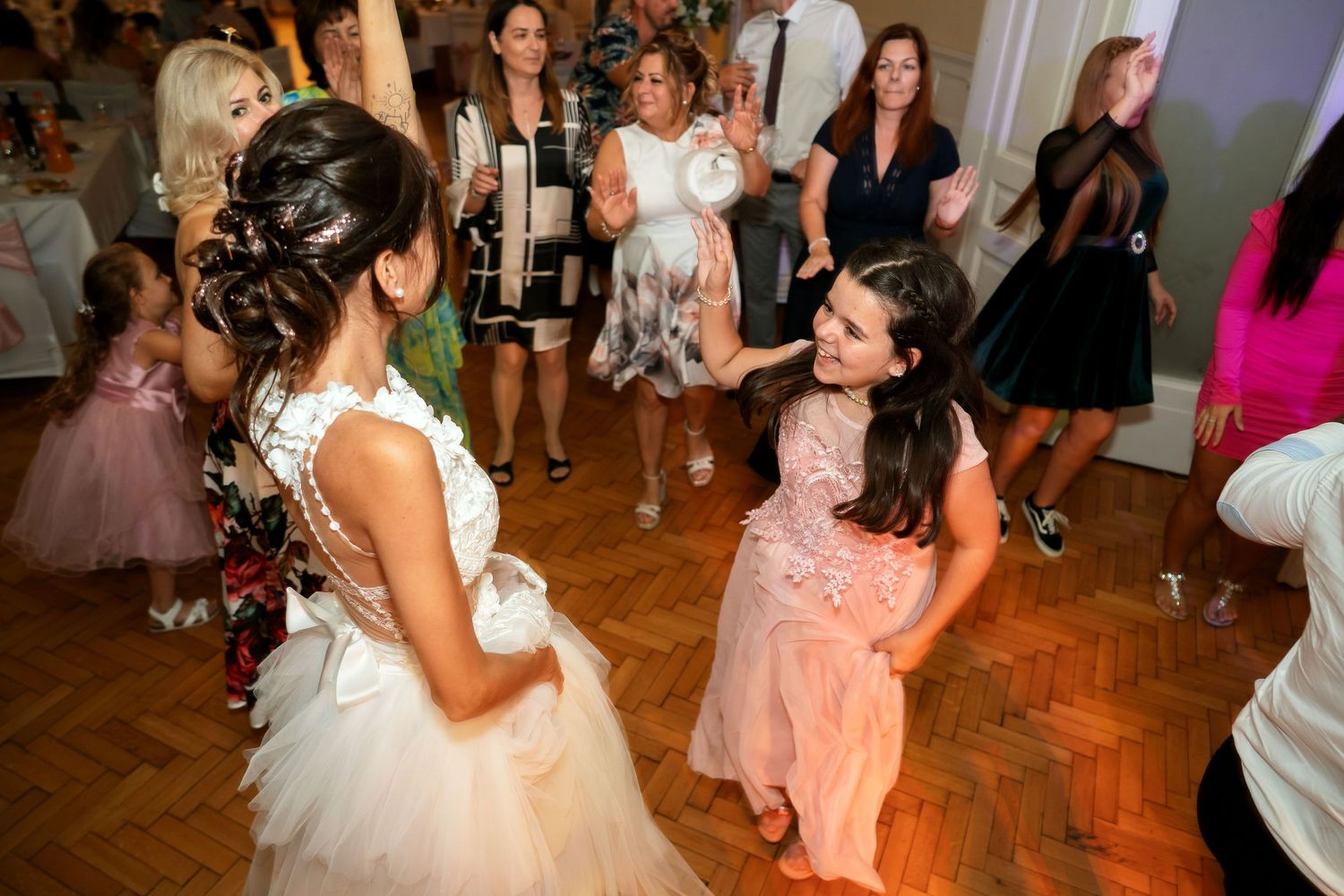 Wedding celebration with guests dancing on a parquet floor in an elegant ballroom.