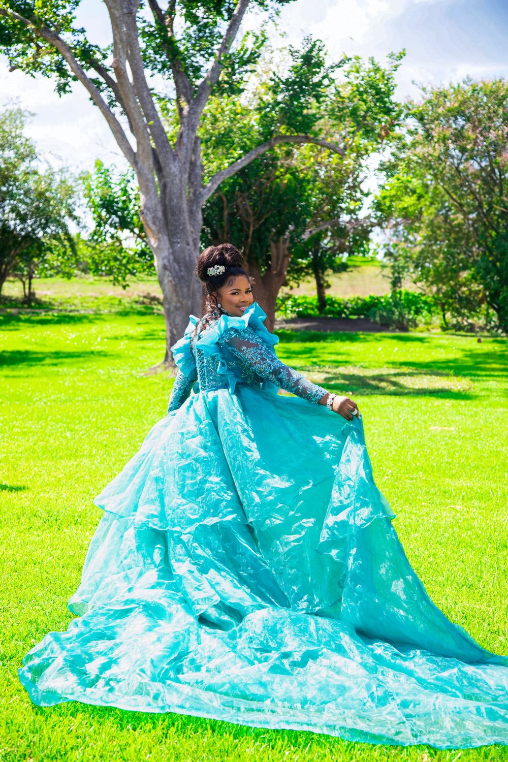 Flowing turquoise gown creates dramatic movement in sunny garden setting.