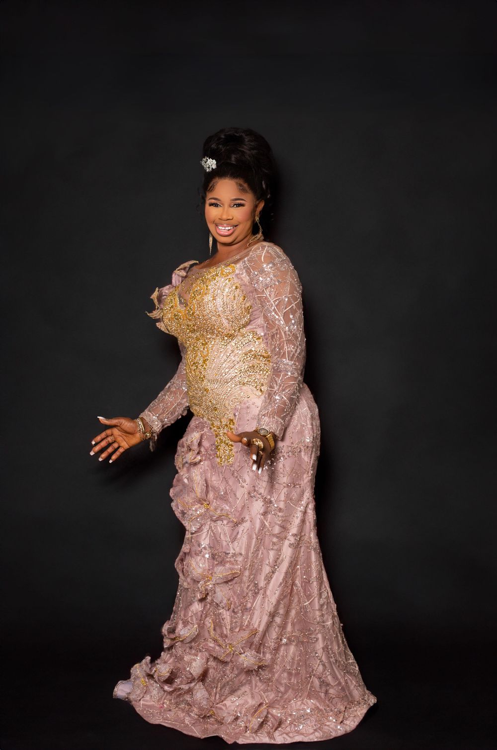 A person in a sparkly pink lace gown poses against a dark backdrop.