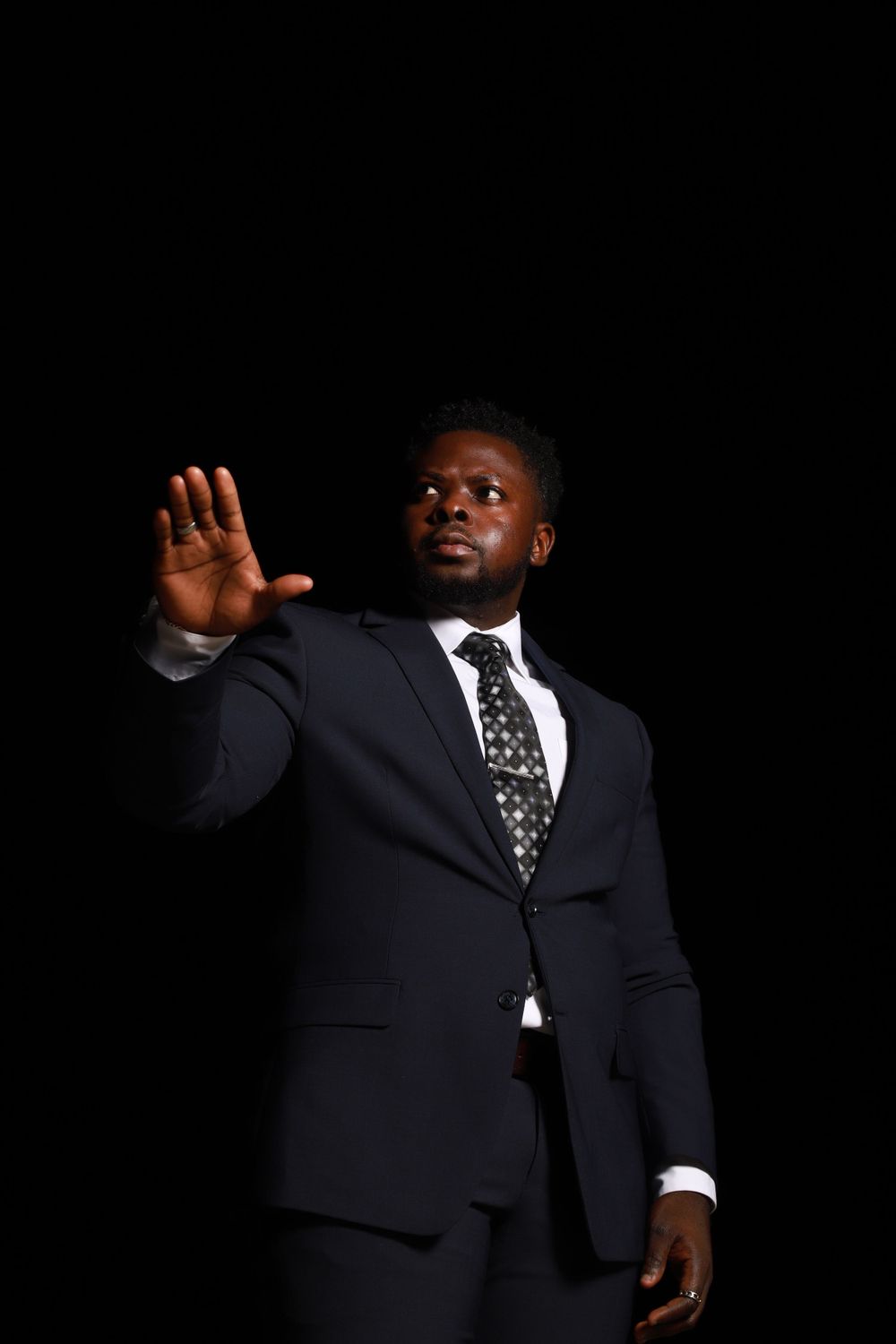 Professional in a dark suit and polka dot tie raising his hand against black background.