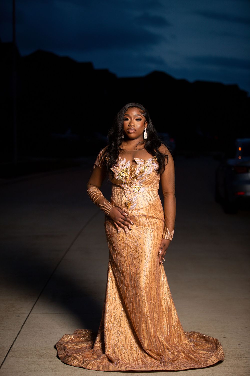 Woman in a shimmering gold evening gown poses for a dramatic nighttime portrait.