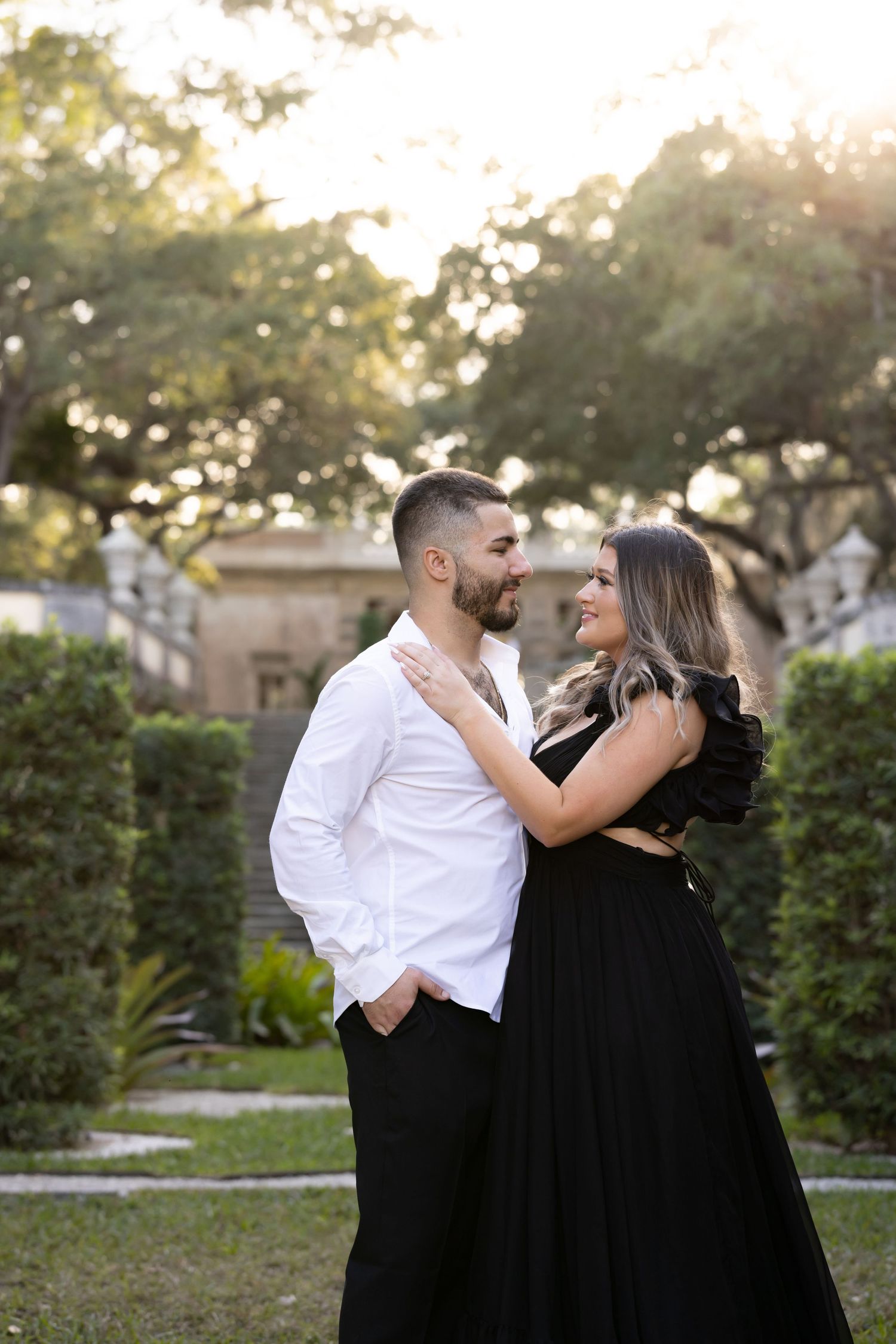 A couple in black and white attire embrace outdoors during golden hour.
