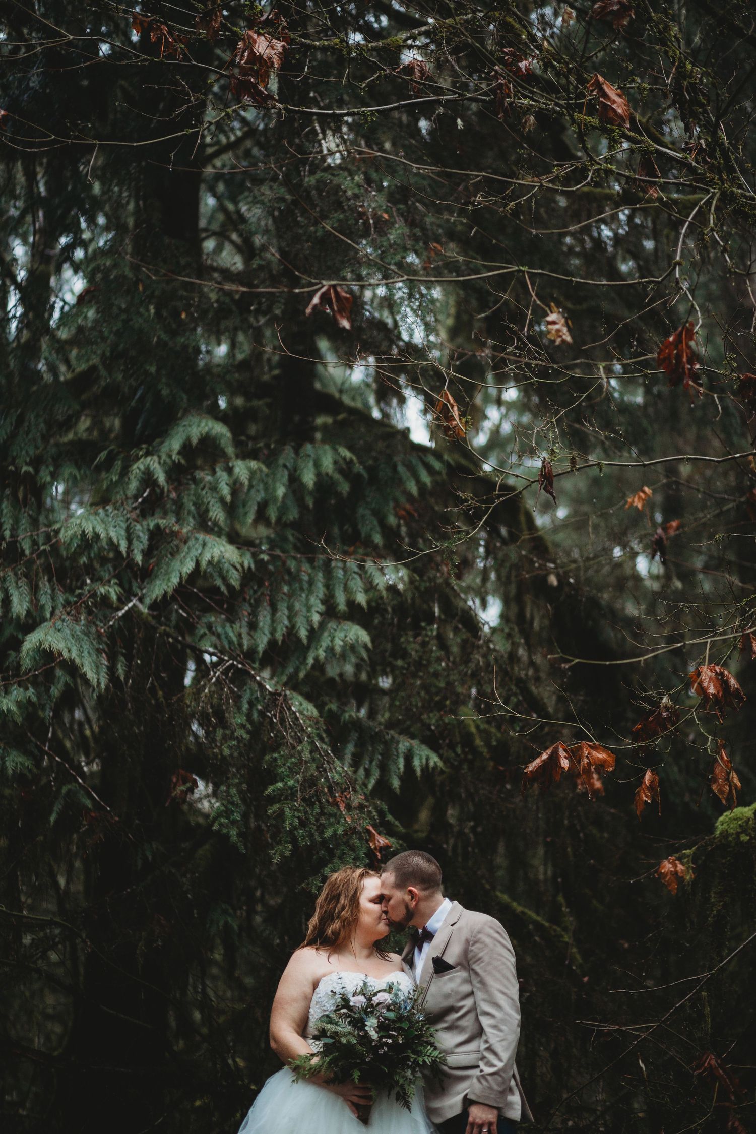 Underneath evergreens and orange fall leaves, a bride and groom kiss at their mountain elopement.