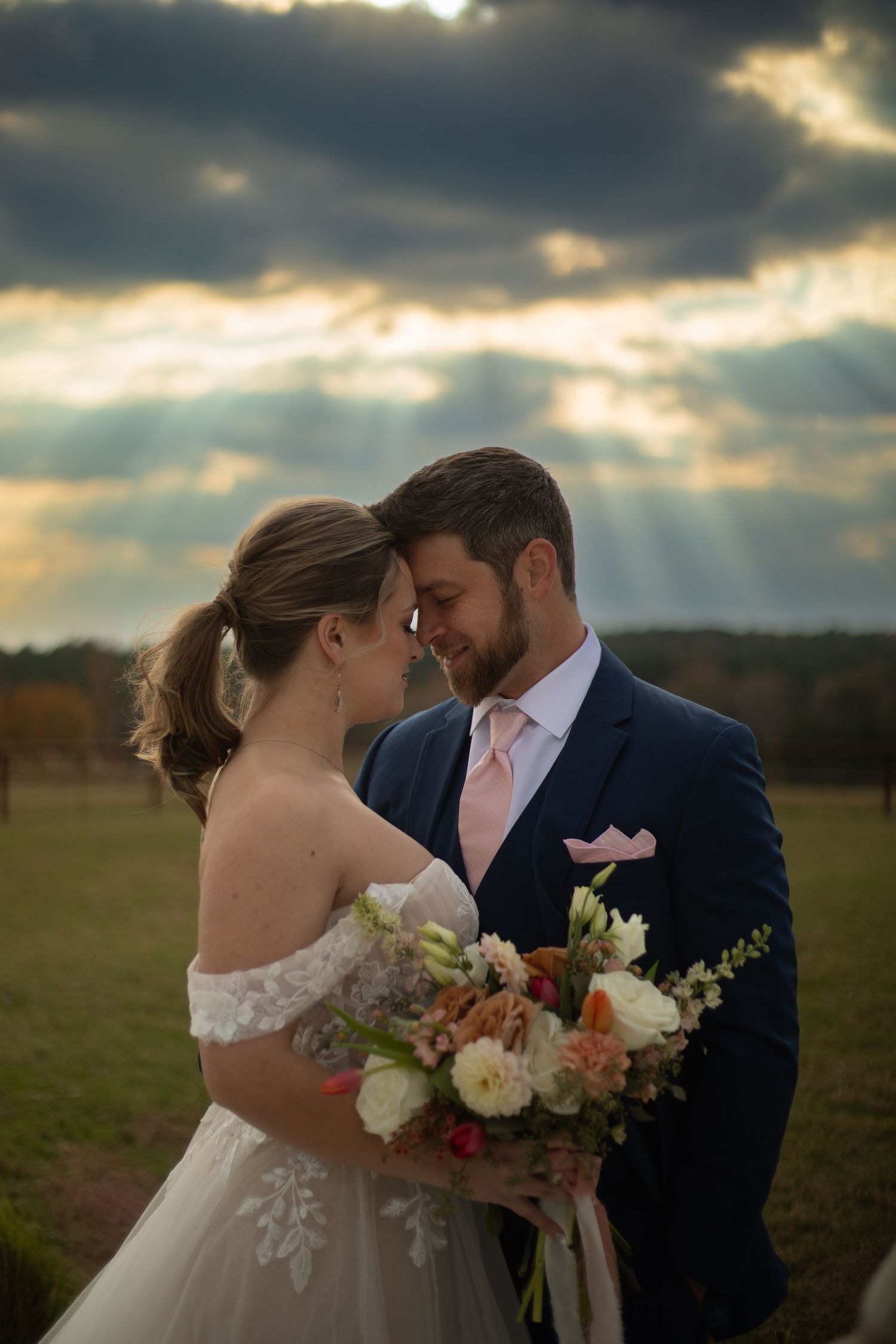 Romantic sunset portrait of couple in wedding attire with dramatic cloudy sky backdrop.